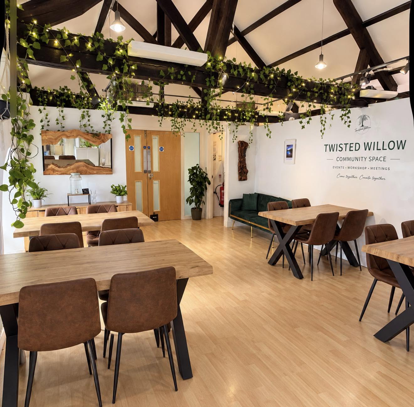 Twisted Willow community space, with its name on the wall, wooden tables, exposed beams and greenery